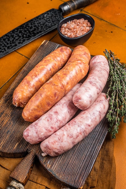 Świeże surowe kiełbaski mięsne Bratwurst i Chorizo na drewnianej desce Pomarańczowe tło Widok z góry