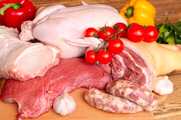 Świeże surowe mięso - wołowina, wieprzowina, kurczak i warzywa na drewnianym tle