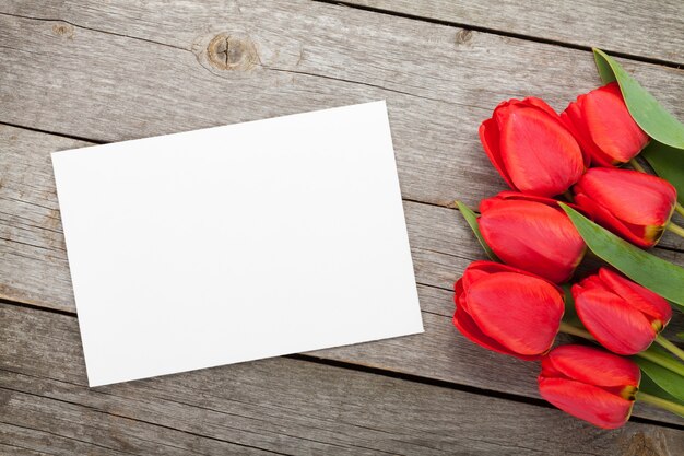 Świeże tulipany i kartkę z życzeniami na drewnianym stole w tle