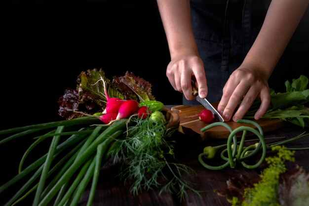 Świeże warzywa cebula zielone rzodkiewka i ręce dziewczyny przygotowuje się na ciemnym tle drewniane w stylu rustykalnym z miejsca na kopię