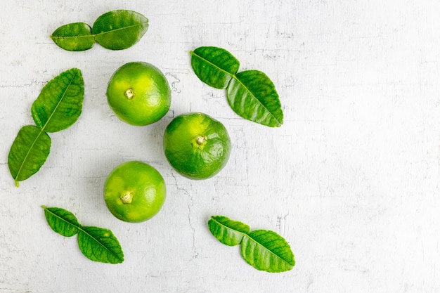 świeże zielone liście limonki i limonki na białym drewnianym stole