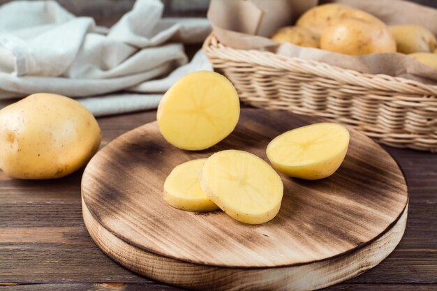 Świeże żółte ziemniaki pokrojone na kawałki na desce i kosz z bulwami na drewnianym stole. Jedzenie wegetariańskie.