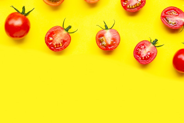 Świezi czereśniowi pomidory, cały i przyrodni cięcie odizolowywający na żółtym tle.
