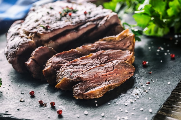 Świeżo grillowany stek wołowy na łupkowej płytce z solą, pieprzem, rozmarynem i ziołami pietruszki. Pokrojone kawałki soczystego steku wołowego.