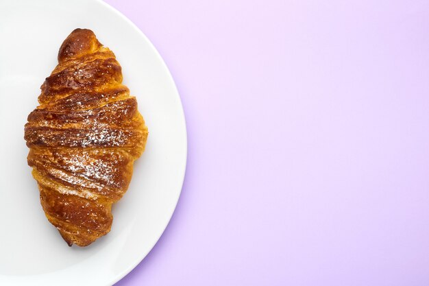 Świeżo piec francuscy croissants na białym talerzu na purpurowym tle z kopii przestrzenią. Pojęcie reklamy tradycyjnego ciasta.