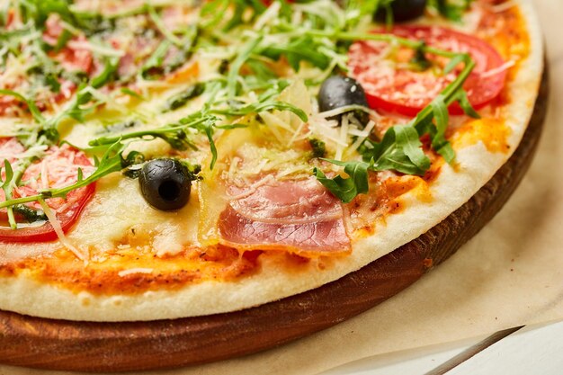 Świeżo upieczona pizza z pesto z szynki rukkola i oliwkami podawana na drewnianym tle z sosami pomidorowymi i ziołami Koncepcja dostawy żywności Menu restauracji