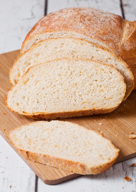 Świeżo upieczony bochenek chleba z kawałkami na desce drewnianej na białej desce