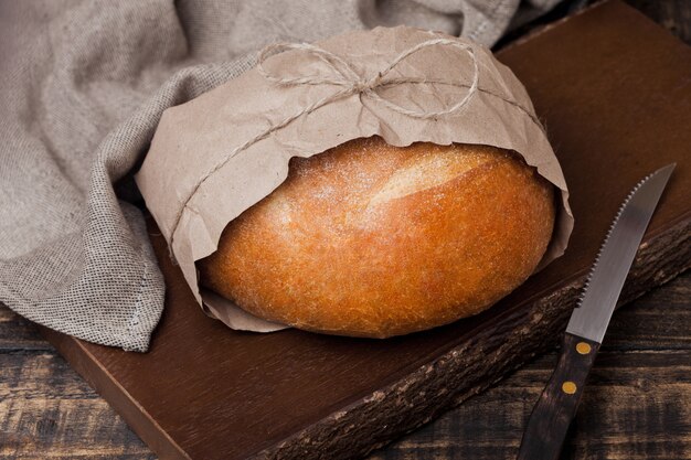 Świeżo upieczony chleb z ręcznikiem kuchennym i nożem na drewnianej desce do krojenia