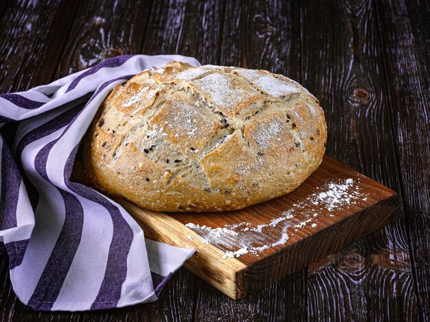 Zdjęcie Świeżo upieczony chleb żytni z nasionami lnu, lniana drewniana taca na ciemnym rustykalnym tle