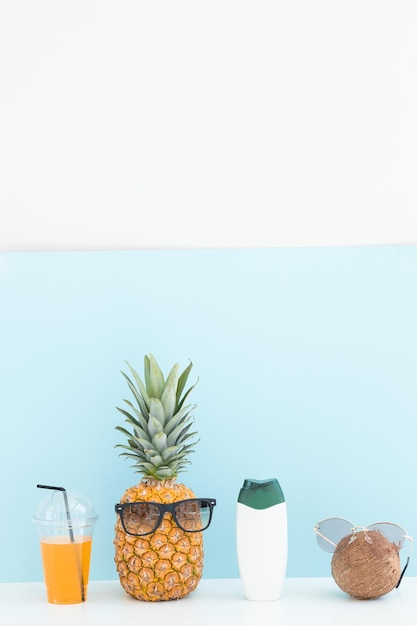 Świeży ananas kokosowy z okularami przeciwsłonecznymi i koktajlową butelką kremu na kolorowym tle
