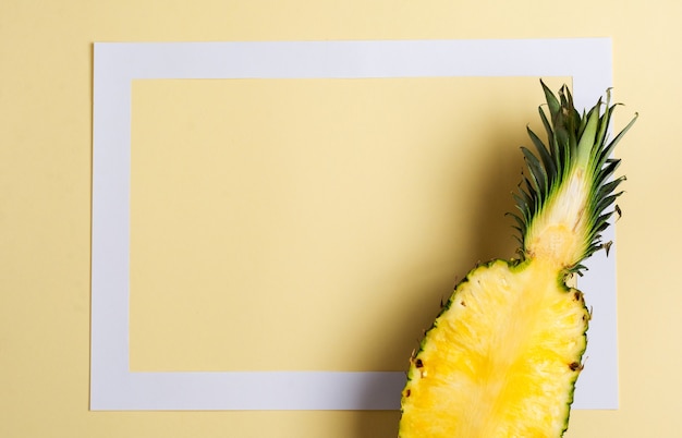 Świeży ananas pokroić w dwie części i papierową ramkę na żółtym tle. Koncepcja lato. Kreatywne mieszkanie leżało z miejscem na kopię. Widok z góry