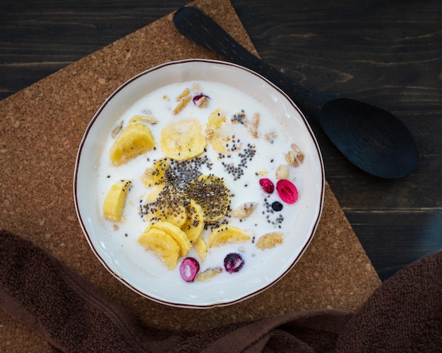 Świeży banan granola z mlekiem w białej misce na brązowym tle posypany nasionami chia