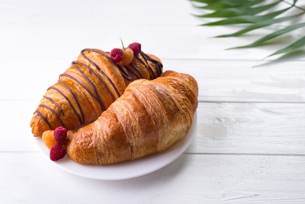 Świeży Croissant z jagodami i palmowym urlopem odizolowywającymi na białym drewnianym tle