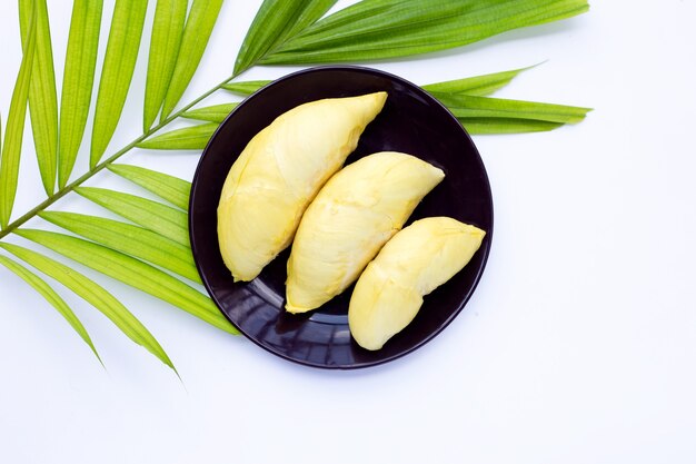 Świeży, dojrzały durian w talerzu na tropikalnych liściach palmowych na białej powierzchni.