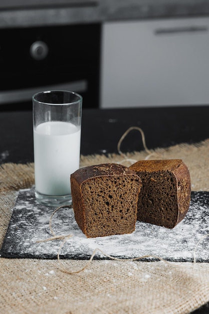 Świeży domowy chrupiący ciemny chleb z nasionami na ciemnym stojaku ze szklanką mleka na ciemnym tle