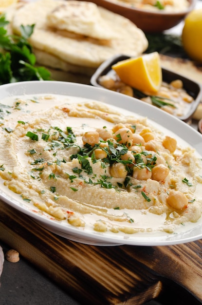 Zdjęcie Świeży hummus domowej roboty w glinianym naczyniu posypany oliwą z oliwek ciecierzycą i posiekanymi liśćmi zielonej kolendry na kamiennym stole podawany z przyprawami