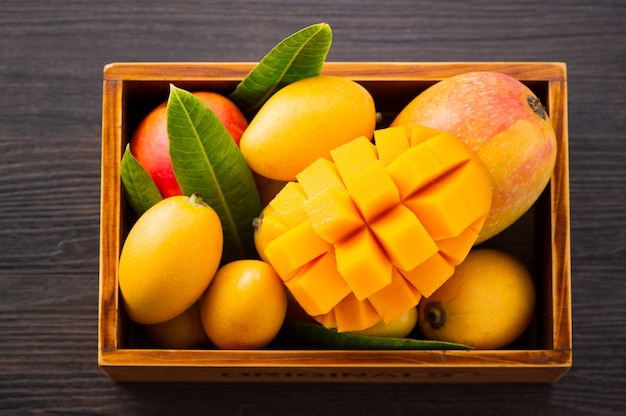 Świeży i piękny zestaw owoców mango w drewnianym pudełku z pokrojonymi w kostkę kawałkami mango na ciemnym drewnianym tle, miejsce na kopię (miejsce na tekst), puste dla tekstu