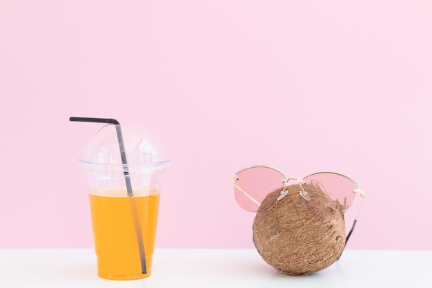 Świeży kokos z okularami przeciwsłonecznymi w pobliżu szklanki soku i słomki koktajlowej na kolorowym tle