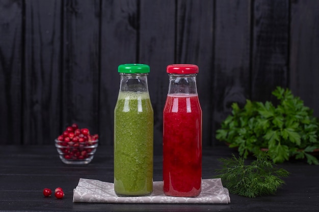 Świeży organiczny czerwony i zielony dwa smoothie w szklanej butelce na czarnym drewnianym stole, z bliska. Orzeźwiający letni napój owocowy. Pojęcie zdrowego odżywiania. Koktajl żurawinowo-malinowy