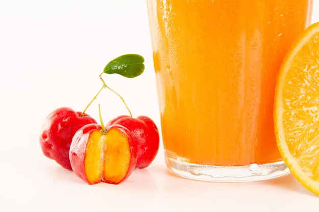 Świeży organiczny sok z aceroli z pokrojonymi owocami aceroli w szklanej filiżance na białym tle i przycięty w widoku z przodu