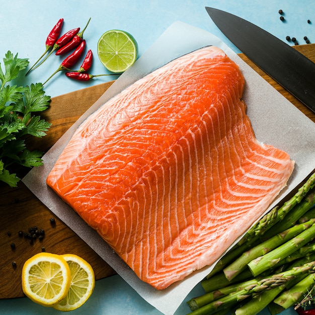 Świeży plasterek łososia na drewnianej desce do krojenia ze świeżymi aromatycznymi ziołami i szparagami na stole. przepis na gotowanie. tło żywności. świeże produkty rybne