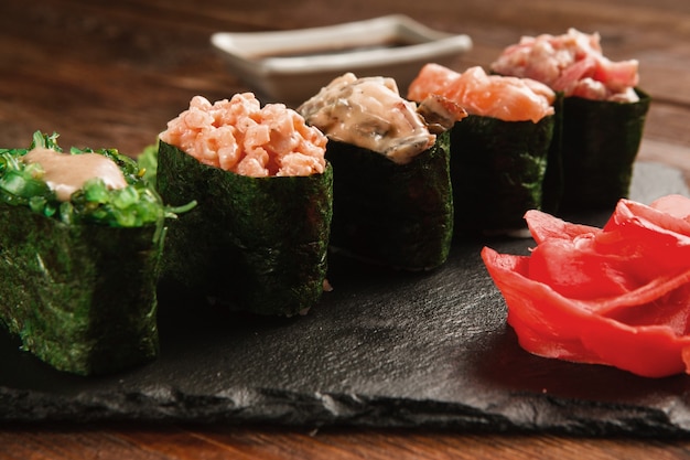 Świeży, pyszny zestaw pięciu sushi gunkan podawany na czarnym łupku z imbirem, zbliżenie. Japońska zdrowa żywność, kuchnia narodowa. Zdjęcie menu restauracji.