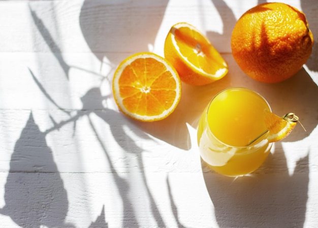 Świeży sok pomarańczowy w szklance przyozdobionej plasterkiem pomarańczy na białym drewnianym stole