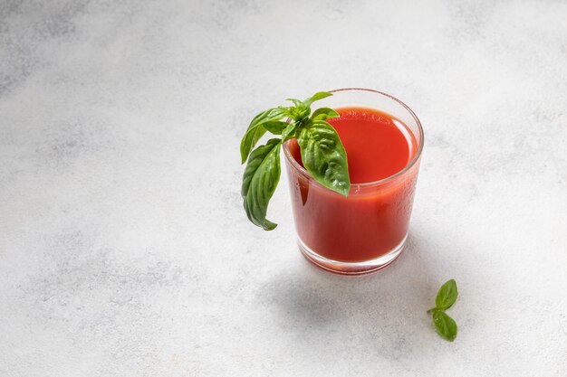Świeży sok pomidorowy z bazylią w szkle na lekkim tle.