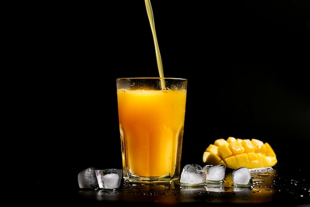 Świeży sok z mango wlewa się do szklanki na czarnym tle
