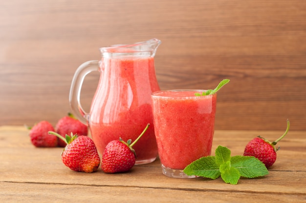 Świeży truskawkowy smoothie z mennicą na nieociosanym drewnianym tle. Zdrowa żywność