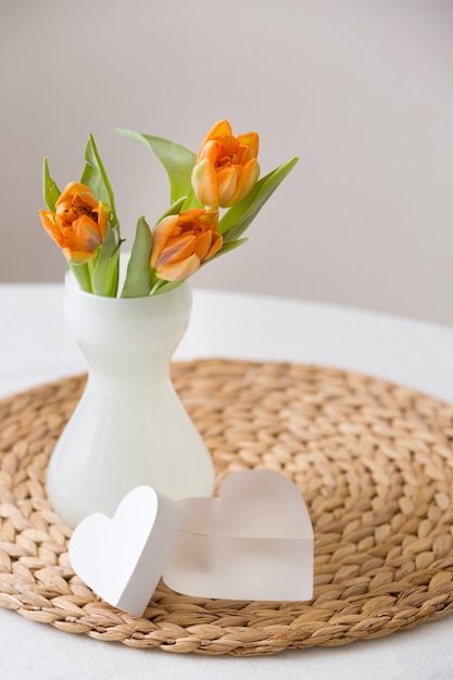 Świeży wiosenny bukiet pomarańczowych tulipanów w ładnym białym szklanym wazonie i dwa słodkie symbole serca