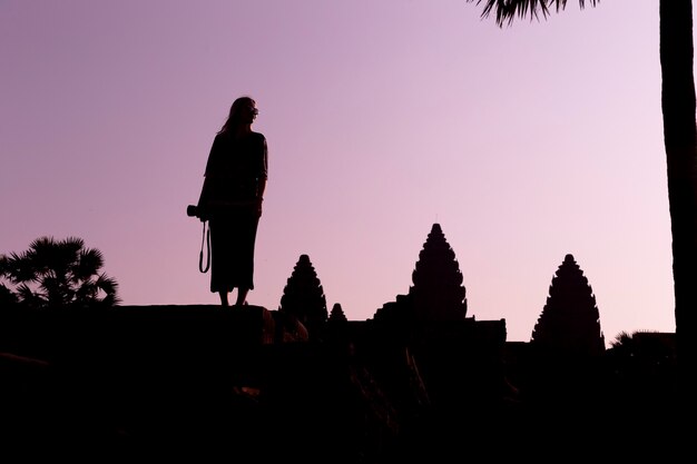 Sylwetka Angkor Wat i dziewczyna podróżnik z aparatem fotograficznym na wschód słońca. Angkor Wat - kompleks świątyń hinduskich w Kambodży