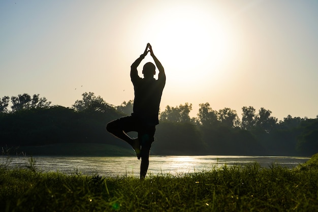 Sylwetka chłopca robi surya namaskar w parku w pobliżu słońca i rzeki - koncepcja zdrowia