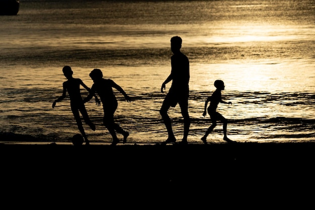Sylwetka czarnych dzieci grających w piłkę nożną na plaży o zachodzie słońca