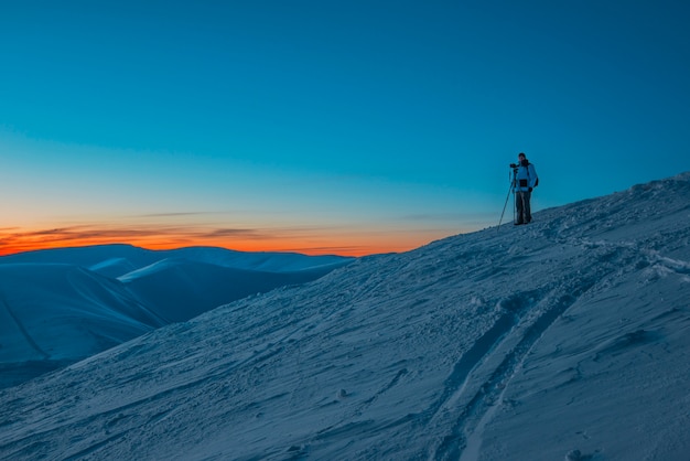 Sylwetka człowieka fotografa stojącego na wzgórzu i robienia zdjęć wieczorem doliny i gór o różowym, kolorowym zachodzie słońca.