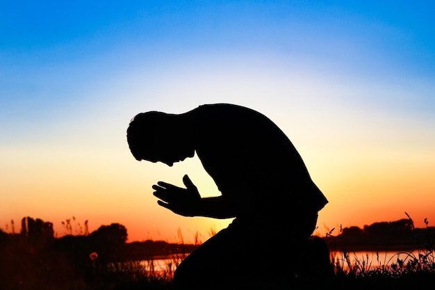 Sylwetka człowieka modlącego się na tle zachodu słońca