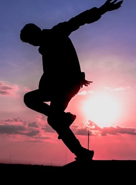 Zdjęcie sylwetka człowieka skaczącego w powietrze z słońcem za sobą