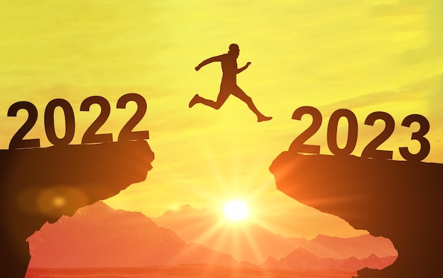 Sylwetka człowieka skacze między 2022 a 2023 rokiem nad słońcem i przez szczelinę wzgórza wieczorne niebo Witamy Szczęśliwego Nowego Roku 2023 Symbol rozpoczęcia i powitania Szczęśliwego Nowego Roku 2023