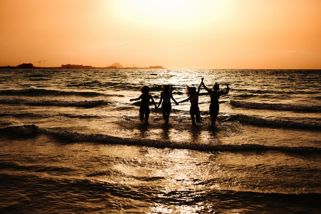 Sylwetka czterech dziewcząt w morzu i trzymając się za ręce.