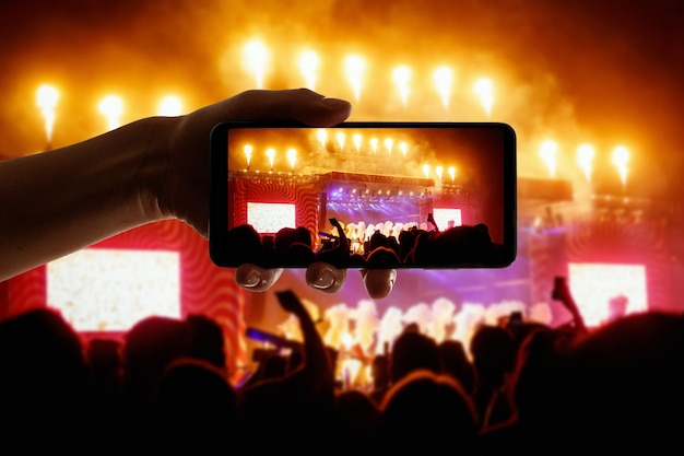 Sylwetka dłoni używającej telefonu z aparatem do robienia zdjęć i filmów na festiwalu koncertów popowych