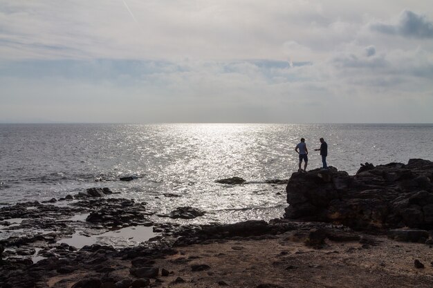 Sylwetka Dwóch Mężczyzn Stojących Na Dużej Skale Nad Oceanem. Lanzarote, Hiszpania.