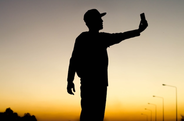 Zdjęcie sylwetka fotografa selfie z zachodem słońca.