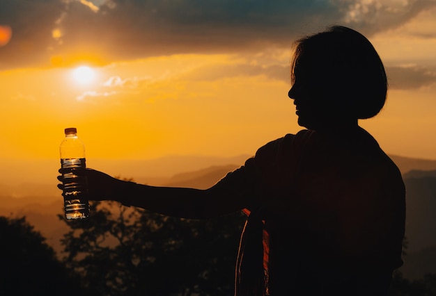 Sylwetka kobiety pijącej wodę pitną o zachodzie słońca