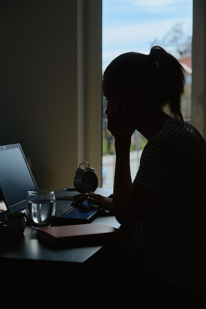 Sylwetka kobiety pracującej zdalnie w domowym biurze z laptopem