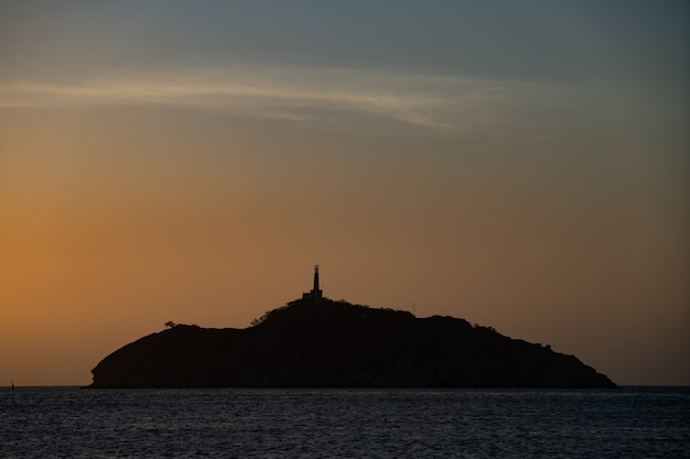 Zdjęcie sylwetka latarni morskiej na szczycie małej skalistej wyspy w morskiej koncepcji podróży i przygody