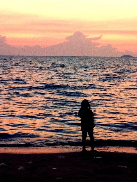 Sylwetka ludzi stojących nad morzem przy zachodzie słońca