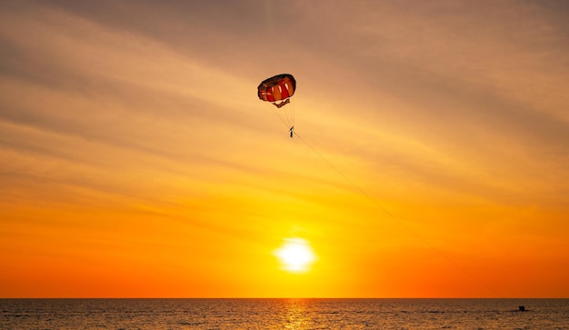 Sylwetka Ludzie podróżujący Parasailing nad morzem Na tle nieba podczas zachodu słońca w złotej godzinie zachodu słońca lub wschodu słońca Aktywna i ekstremalna rekreacja