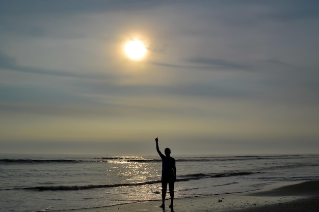 Sylwetka mężczyzny unoszącego lewą rękę na brzegu plaży o zachodzie słońca Ocean Spokojny Peru