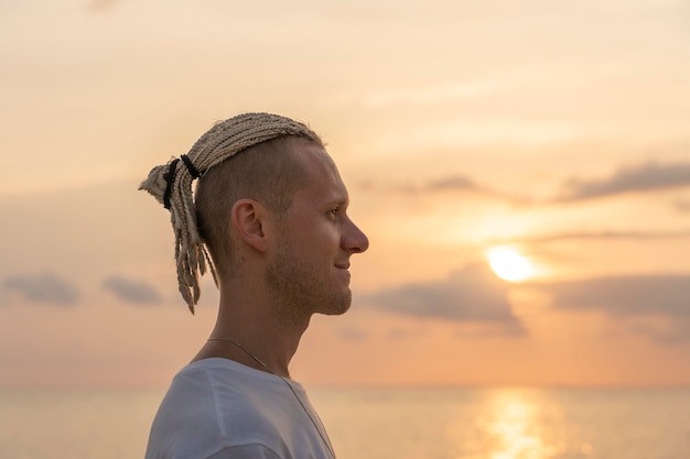 Sylwetka młodego faceta z dredami na głowie w pobliżu morza podczas zachodu słońca Portret z bliska Szczęśliwy przystojny mężczyzna z dredami na tropikalnej plaży