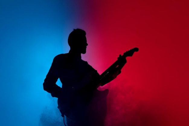 Sylwetka młodego kaukaskiego gitarzysty męskiego odizolowanego na niebiesko-różowym studio gradientowym w świetle neonowym